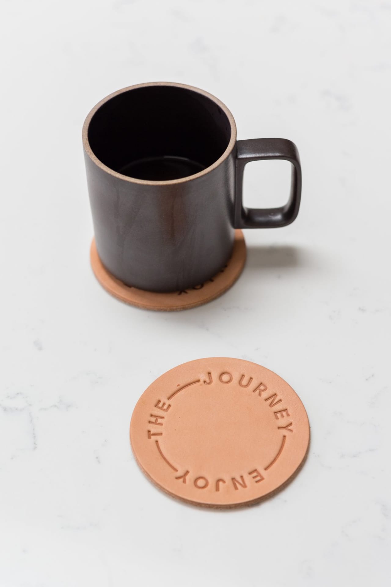 Circular leather coaster set with natural color and "Enjoy the Journey" embossed type.