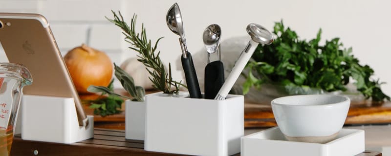 Walnut organizer base with white polycarbonate trays in the kitchen with various kitchen utensils.